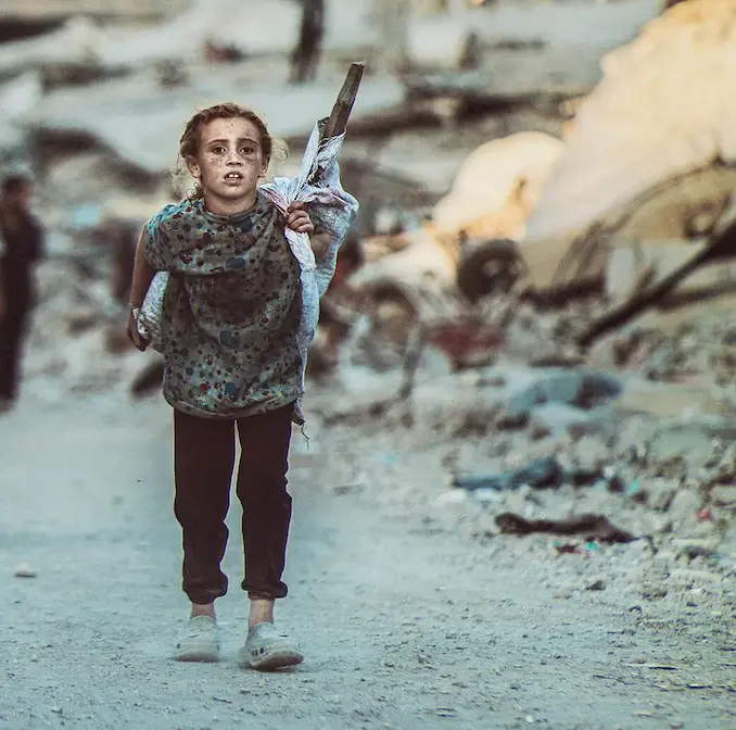 Et barn går alene gennem et krigsramt område omgivet af ruiner, der symboliserer behovet for UNICEF’s nødhjælp og beskyttelse af børn i konfliktzoner.