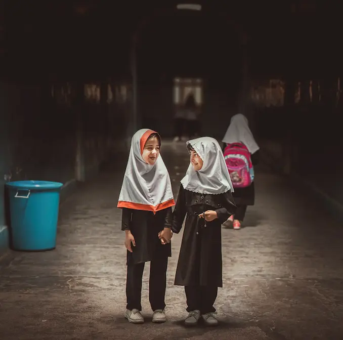 To piger med skolebøger går sammen på vej mod undervisning, et symbol på UNICEF’s indsats for at sikre pigers ret til skolegang.